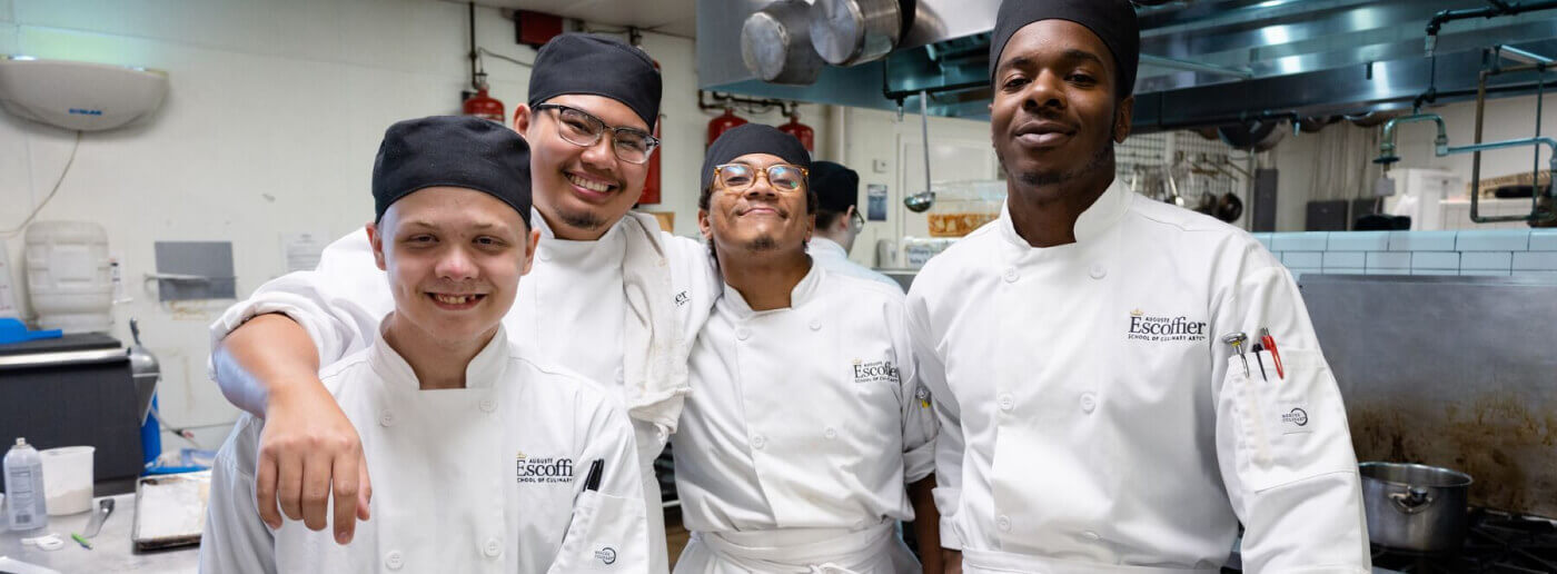 Four Escoffier Austin campus students smiling and looking towards the camera
