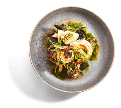 A plated seafood stew with squid, clams, and shrimp in a stone bowl