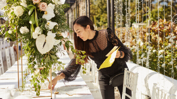 An event planner puts the finishing touches on a table setting at an outdoor wedding reception
