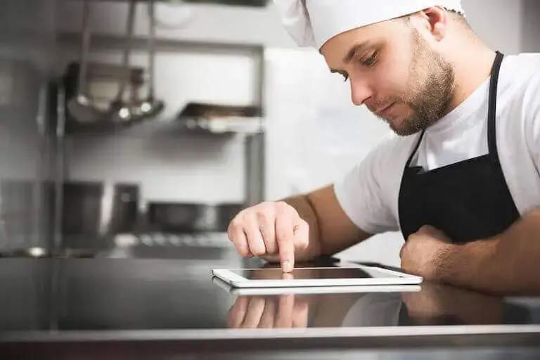 Person in a professional kitchen scrolls on a tablet.