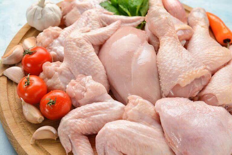 Raw chicken pieces, cleanly trimmed on a cutting board surrounded by tomatoes, peppers, and lettuce.