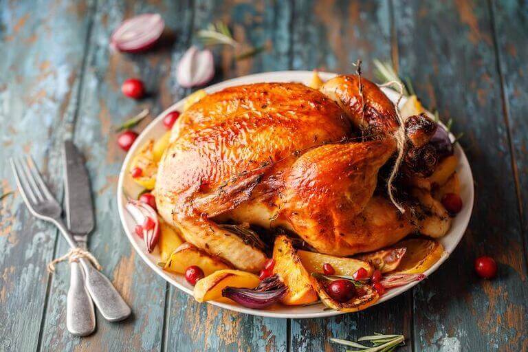 Roasted chicken with the legs trussed on a white plate with grilled, sliced citrus fruit and cranberries.
