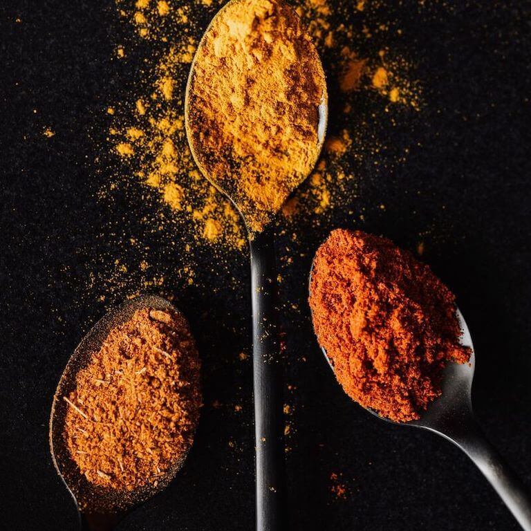 Three varieties of seasonings with different hues of red and orange on spoons.