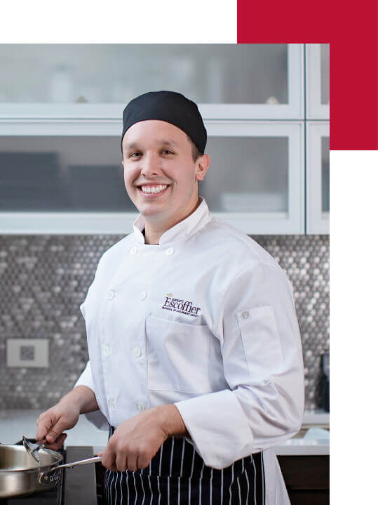 A male Escoffier online culinary arts student smiles at the camera while cooking in his home kitchen