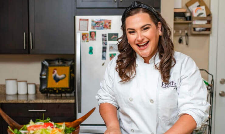 Food stylist and Escoffier online culinary arts graduate Lisa Spychala cooking in her kitchen and smiling at the camera