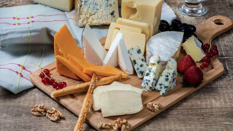 A cheese board with different types of cheeses, fruit, nuts, and a couple of pretzel rods.