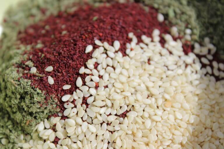 A closeup image of ground oregano, ground sumac, and sesame seeds.