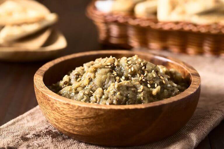 A wooden bowl of roasted eggplant has a sprinkle of za’atar spice blend on top.