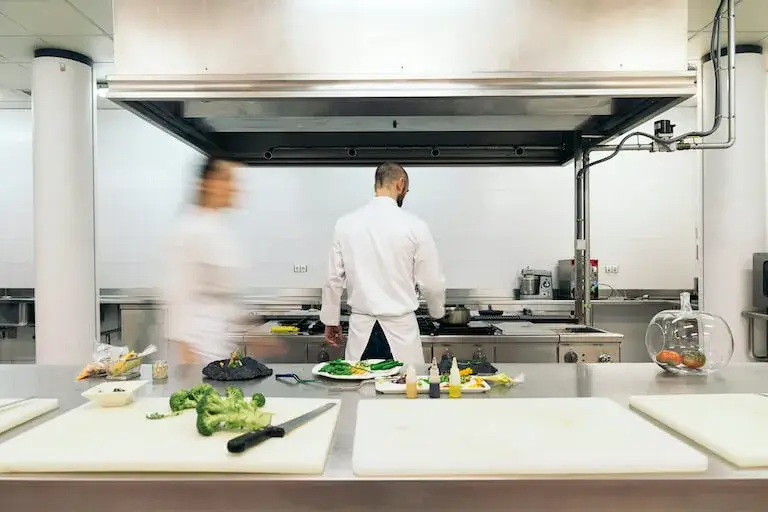 Two chefs in white uniforms working at a stovetop in a busy professional kitchen.