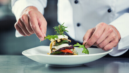 a chef garnishes a plant-based entree with arugula and rosemary