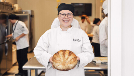 an Escoffier culinary student proudly holds a fresh baked sourdough boule