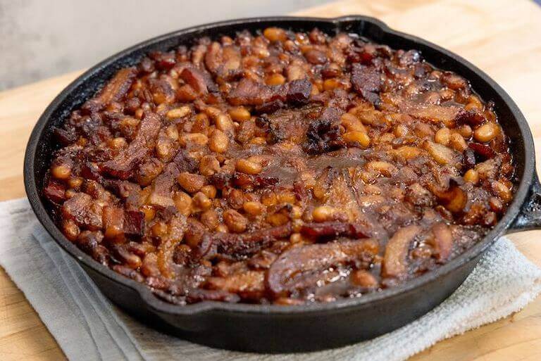 A large batch of Boston baked beans sits in a large cast iron skillet.