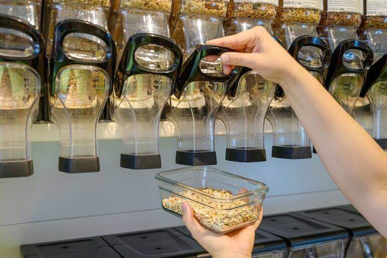 A person dispenses bulk rolled oats into a glass container for purchase at a grocery store. 
