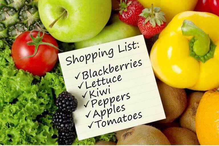 A short grocery list is shown on a post it note in front of a background of fresh, colorful vegetables.