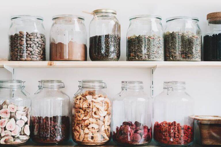 Two shelves hold rows of airtight glass jars filled with dried ingredients like beans and dried fruit.