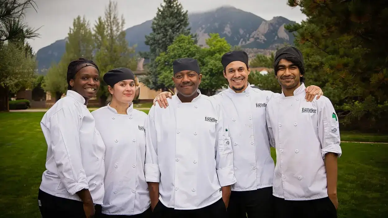 A group of Escoffier culinary students in chef coats posing in a scenic Boulder setting