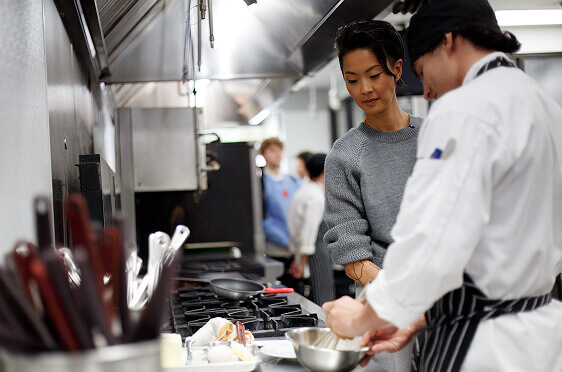 Kristen Kish watching escoffier student whisk eggs in Escoffier classroom kitchen