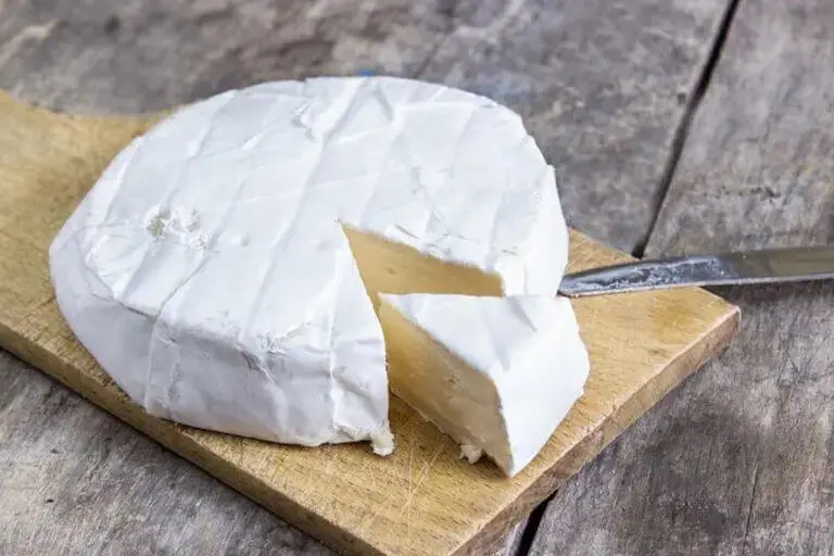 A wheel of brie cheese on a cutting board with a wedge cut out of it.