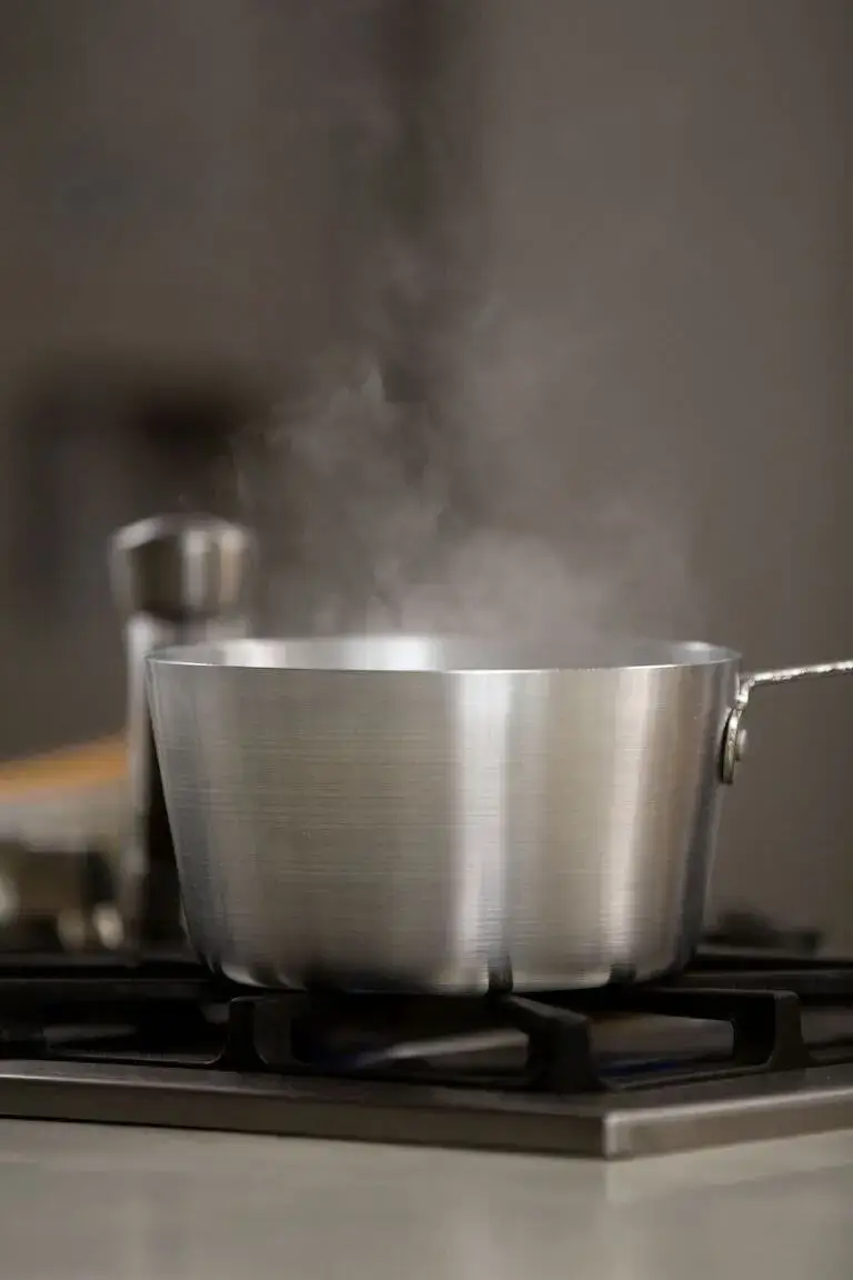 Close-up of a stainless steel pot on a gas stove, emitting steam while boiling water.