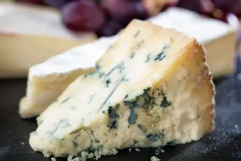 Closeup view of a wedge of stilton cheese on a black cutting board.