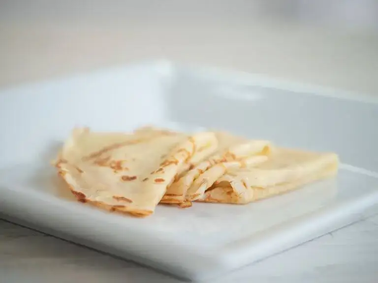 Crepes folded and stacked on a white plate.