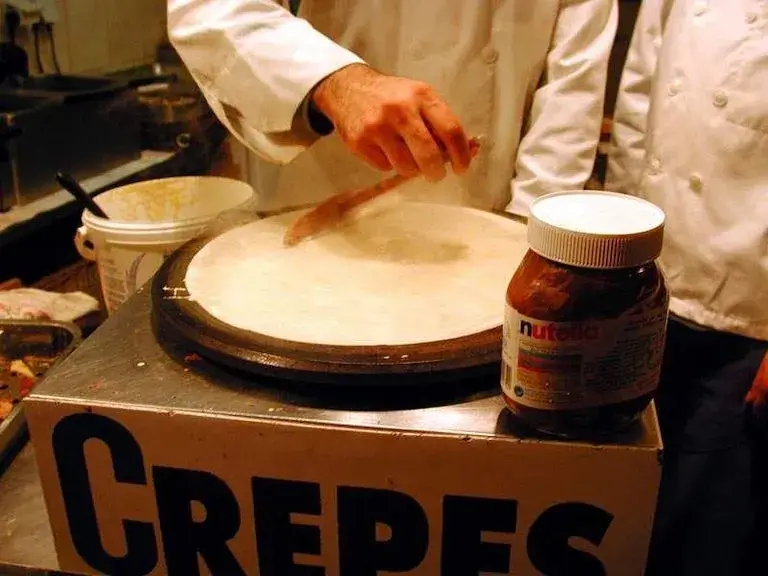Hand holding a wooden spreader preparing a crepe.