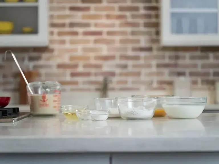 The ingredients to make crêpes prepared in glass bowls on a white countertop.