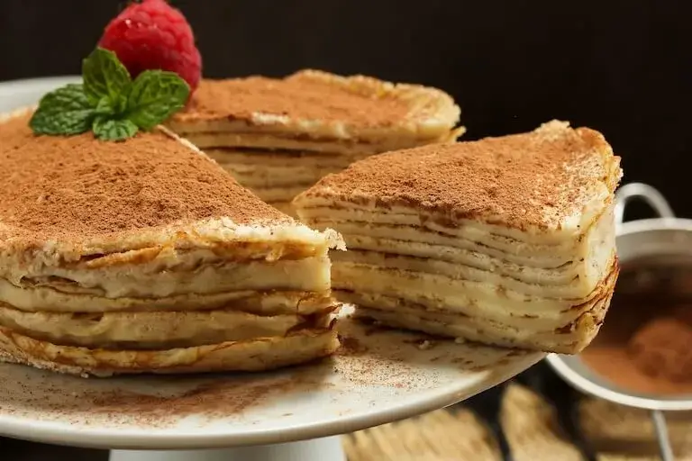 Tiramisu Crepe Cake topped with raspberry and cocoa powder.
