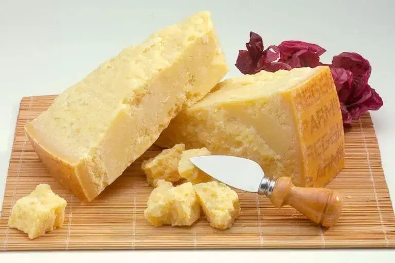 Two blocks of Parmigiano-Reggiano cheese on a wooden cutting board with a small cheese knife.