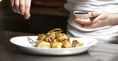 Chef adding final garnish to a plated gourmet dish in a professional kitchen