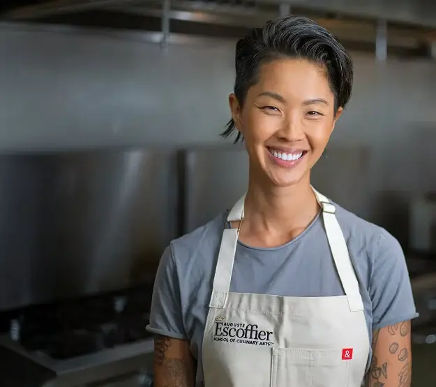 Escoffier Chef-in-Residence Kristen Kish, wearing an Escoffier apron, smiles in an Escoffier kitchen setting