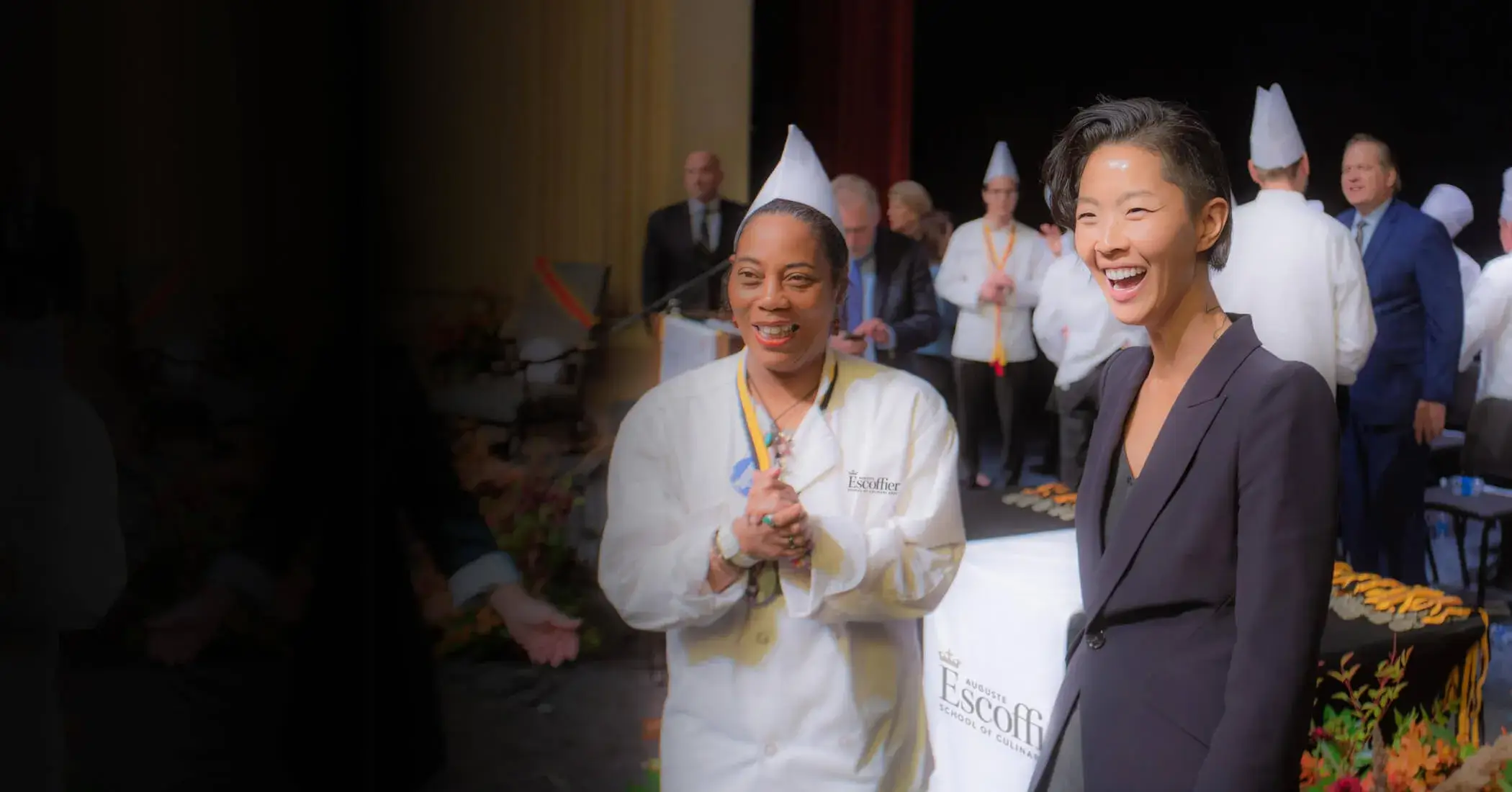 Kristen Kish stands with an Escoffier graduate at the graduation. Both are looking at something off-camera and smiling.
