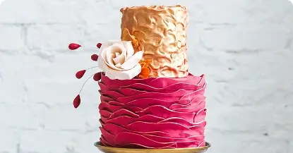 Elegant pink and gold wedding cake with intricate details and a sugar rose