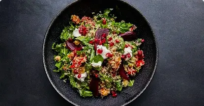 Healthy quinoa salad with pomegranate, greens, and goat cheese in a black bowl