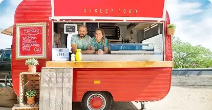 Two food truck owners leaning on their red mobile kitchen, ready to serve customers