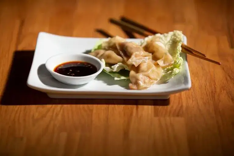 A plate of water dumplings garnished with lettuce and served with soy sauce, with chopsticks resting beside on a wooden table.