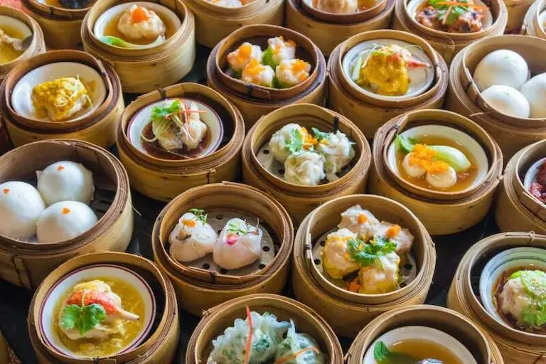 Assorted dim sum in bamboo steamers, featuring various dumplings and buns, garnished with vibrant accents.