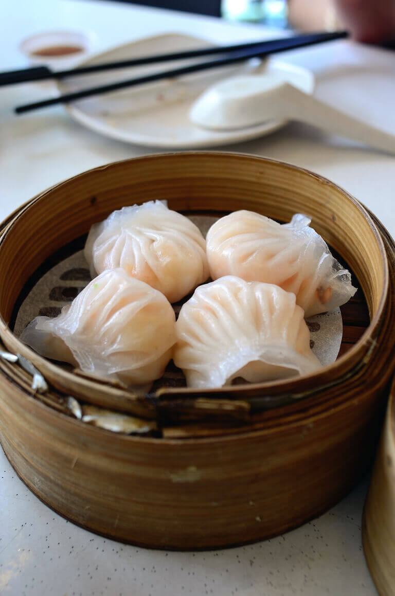 Close-up of translucent Har Gow shrimp dumplings in a bamboo steamer, with chopsticks resting in the background.