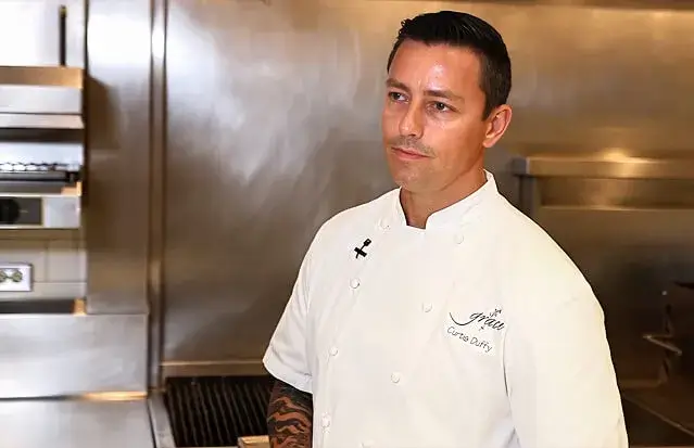 Escoffier Partner and Michelin-starred Chef Curtis Duffy stands in a professional kitchen wearing a white chef coat