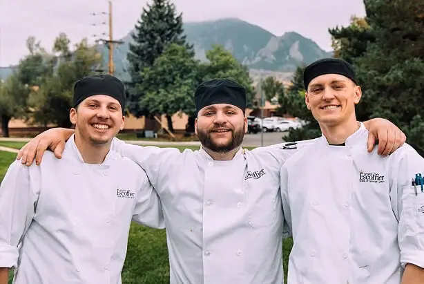 ree male Escoffier culinary students smiling outdoors in chef coats with mountain view