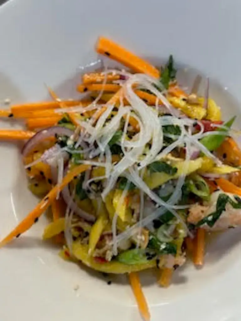 A plated salad with julienned carrots, red onion, herbs, and thinly sliced white vegetables in a white bowl.