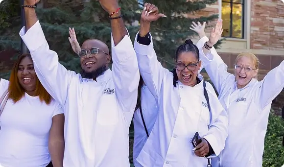 Group of diverse Escoffier culinary students in uniform raising hands and smiling outdoors