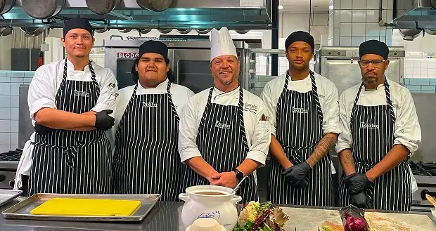 Escoffier culinary students and a Chef Instructor in aprons posing in an Escoffier kitchen