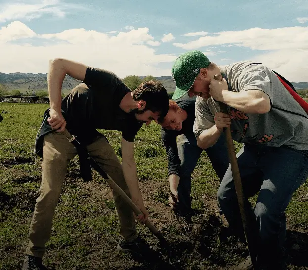 Three Escoffier culinary students working together to dig in a farm field with mountains in the background.