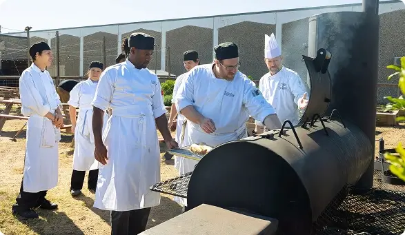 Escoffier culinary students and chef instructor grilling at an outdoor barbecue cooking lesson