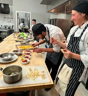 Escoffier culinary students focused on plating desserts at a prep counter during pastry class