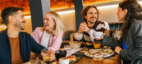 Group of friends enjoying food and drinks together at a cozy restaurant table, laughing and socializing
