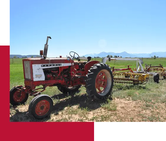 Vintage red Farmall tractor parked in a green field with the Rocky Mountains in the background