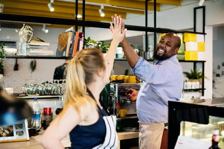Two restaurant employees high five in a restaurant kitchen.
