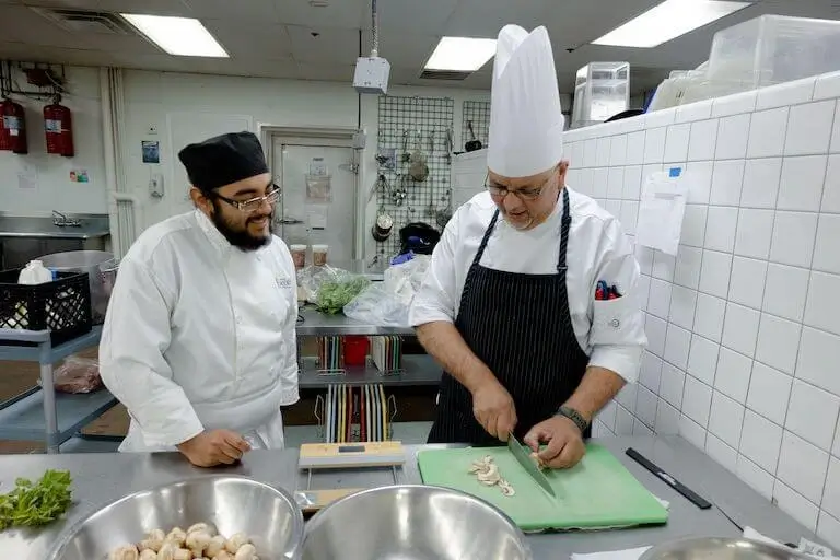 Chef Miguel Olmedo helps a student plate a dish in a teaching kitchen at Escoffier.